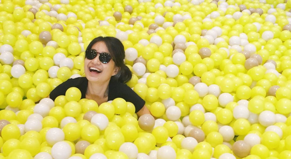 Woman smiling in a yellow ball pit wearing sunglasses Woman smiling in a yellow ball pit wearing sunglasses